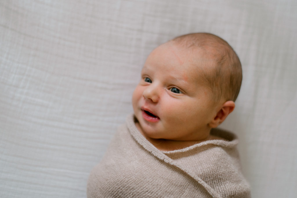 Close up of infant boy in beige swaddle.