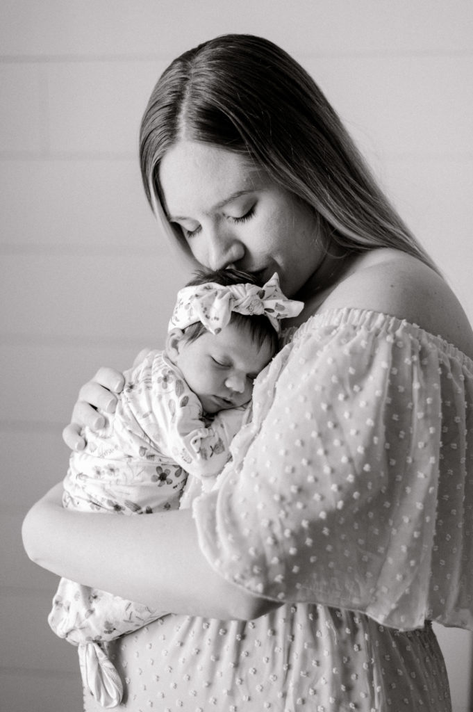 Black and white of new mom kissing the top of her newborn girls head while holding her chest to chest