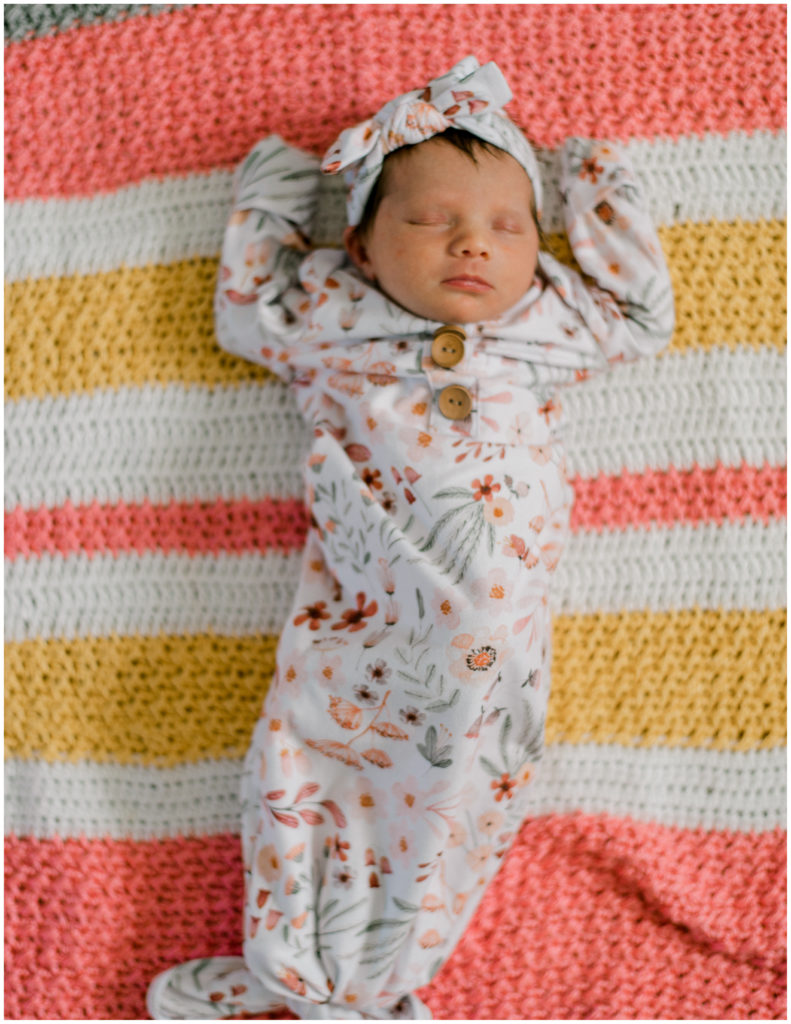 Newborn girl laying on a pink white and yellow crochet baby blanket
