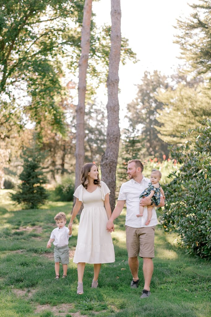A mom and dad walking hand in hand with their two young children through a garden, while smiling and looking at each other for a Schoepfle Gardens family session by Brittany Serowski Photography.
