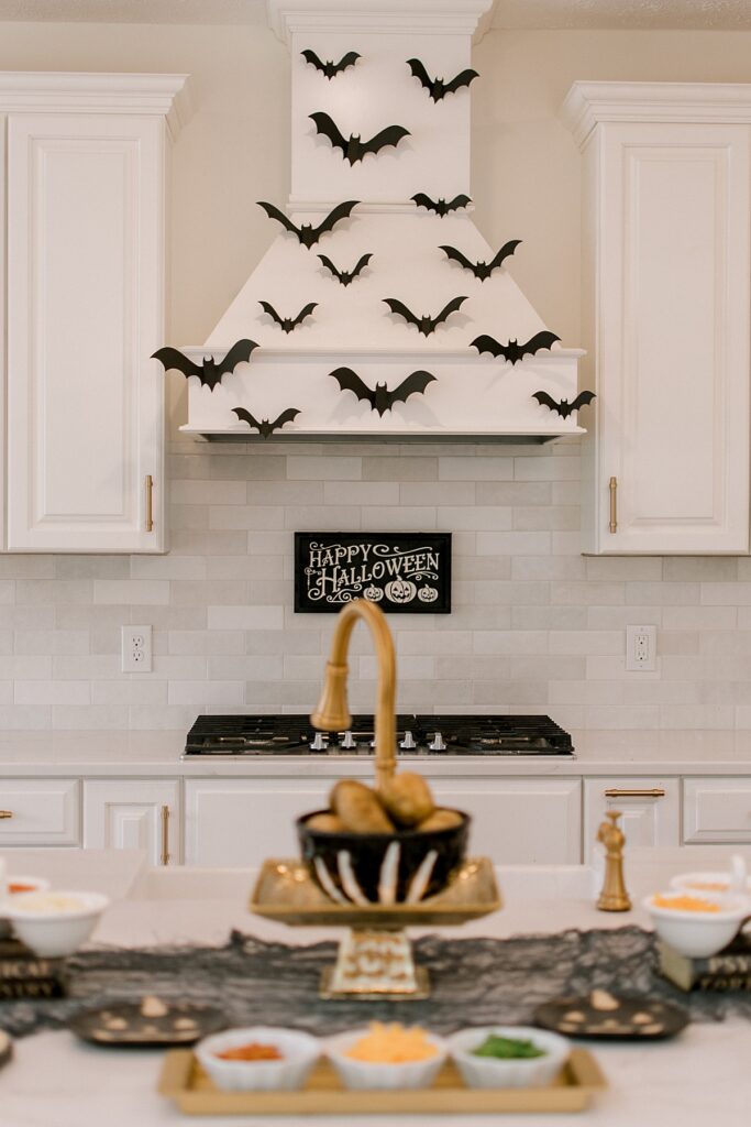 An all white kitchen decorated for Halloween hosting with paper bats on the vent hood ready for hosting a memorable Halloween. Party styling and design by One Stylish Party, Photographed by Brittany Serowski Photography.