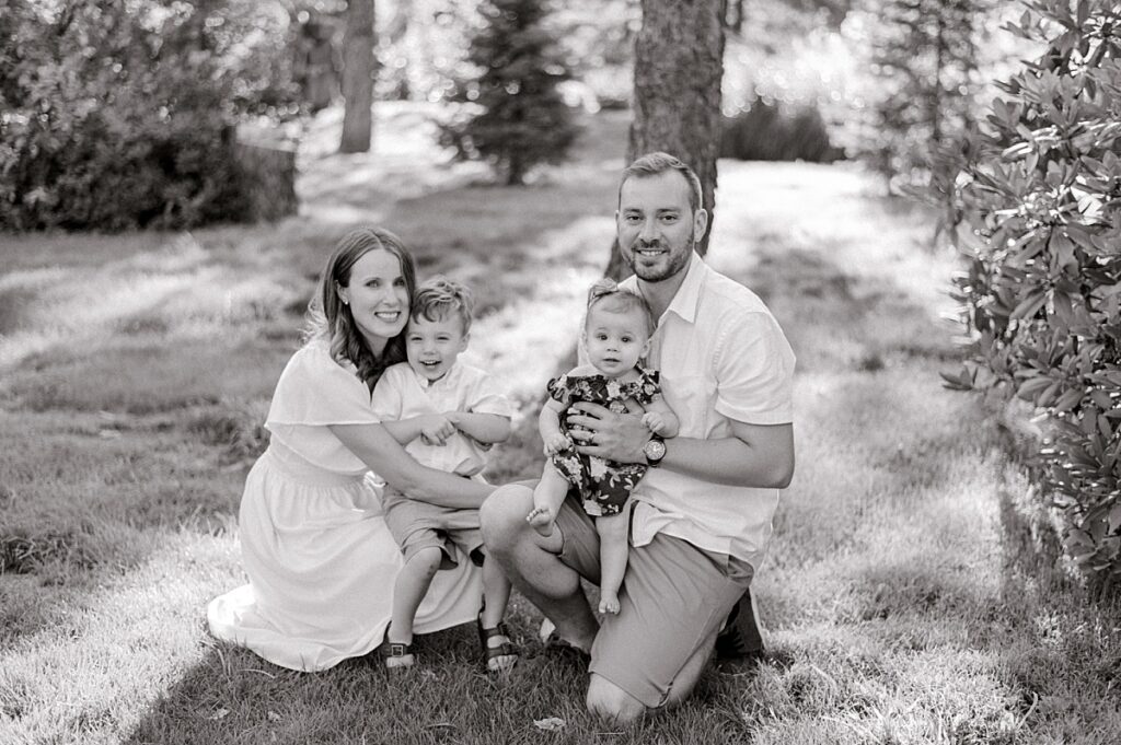 A family of four kneeling next to their children while smiling and looking at the camera in a black and white photo for a Schoepfle Gardens family session by Brittany Serowski Photography.