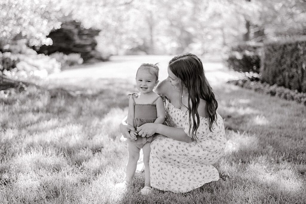 A Schoepfle Gardens summer maternity session by Brittany Serowski Photography with a mom kneeling down next to her young daughter under a big tree.