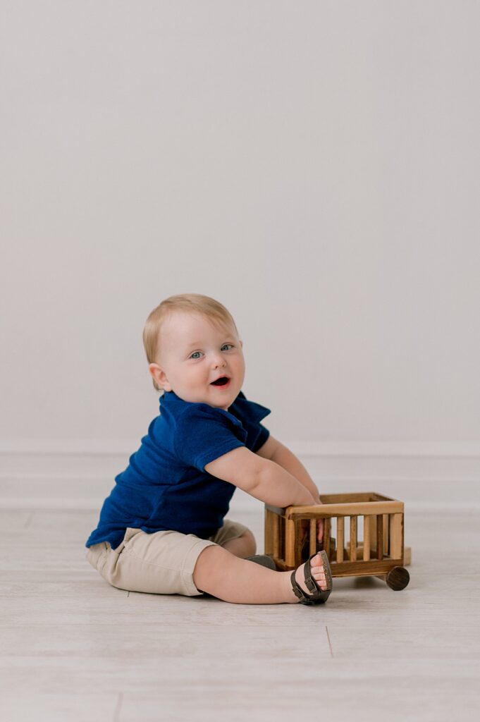 A one year old boy  playing with a wooden toy at Lake Arts Studio while laughing at the camera by Cleveland Milestone Photographer, Brittany Serowski Photography.