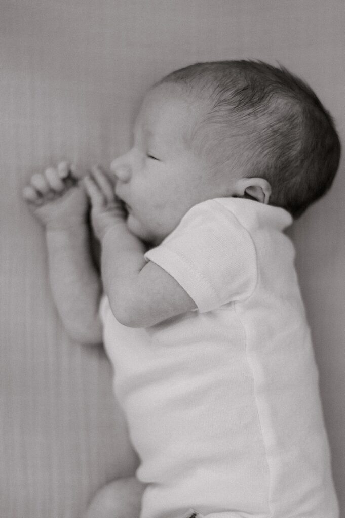 A newborn boy in a black & white picture with a white onesie on a sheet sleeping by Cleveland Newborn Photographer, Brittany Serowski Photography.