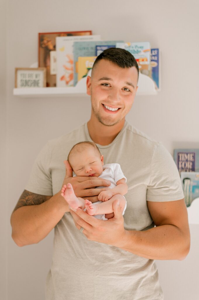 A new dad holding his newborn son in a white onesie, smiling at the camera by Cleveland Newborn Photographer, Brittany Serowski Photography.