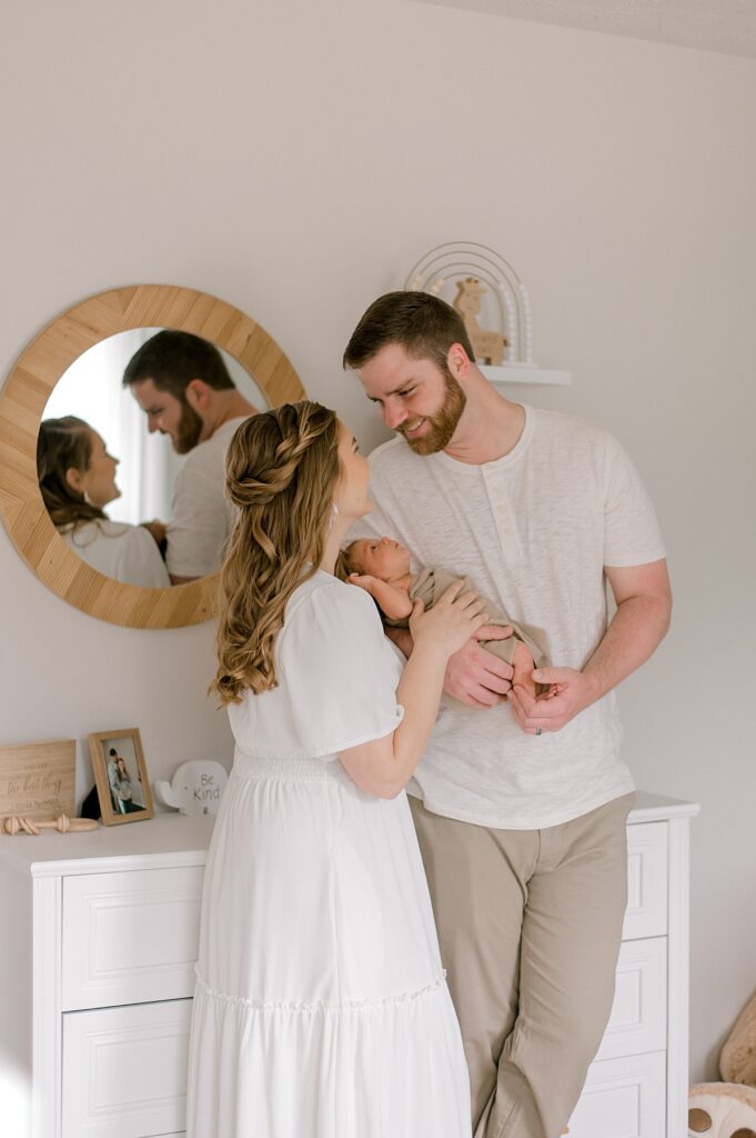 A Medina neutral nursery session by newborn photographer, Brittany Serowski Photography. A new mother and father looking at each other while cuddled close to their newborn son, in their son's nursery.