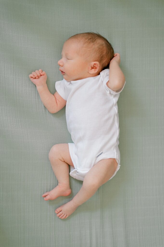 A newborn boy in a white onesie on a green sheet sleeping by Cleveland Newborn Photographer, Brittany Serowski Photography.