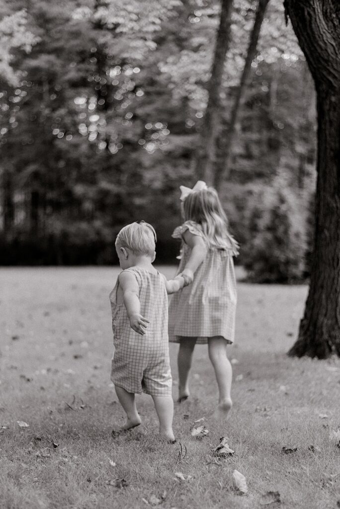 A brother and sister duo holding hands, running off into their backyard by Chagrin Falls Family Photographer, Brittany Serowski Photography.