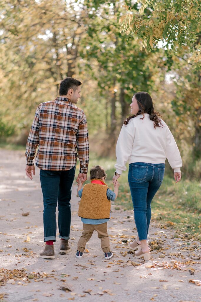 A family of three holding hands and walking away down a gravel path while mom and dad look at one another smiling by Cleveland fall family photographer, Brittany Serowski Photography.