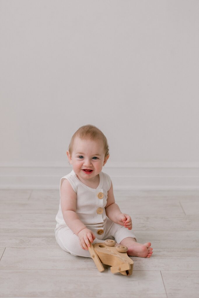 A 6 month old baby in a neutral romper with wood buttons in front of an all white background at Lake Arts Studio, smiling at the camera by Cleveland Personality Portraits photographer, Brittany Serowski Photography.