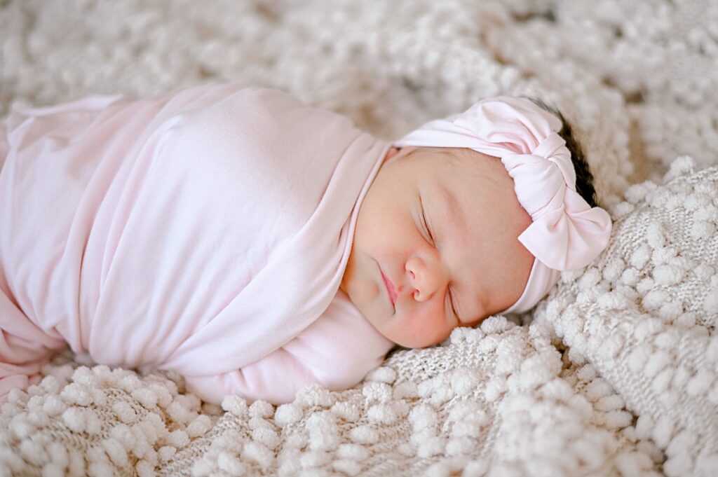 A newborn girl swaddled in a pink swaddle on top of a chunky knit cream blanket, while sleeping soundly by Cleveland Newborn Photographer, Brittany Serowski Photography.