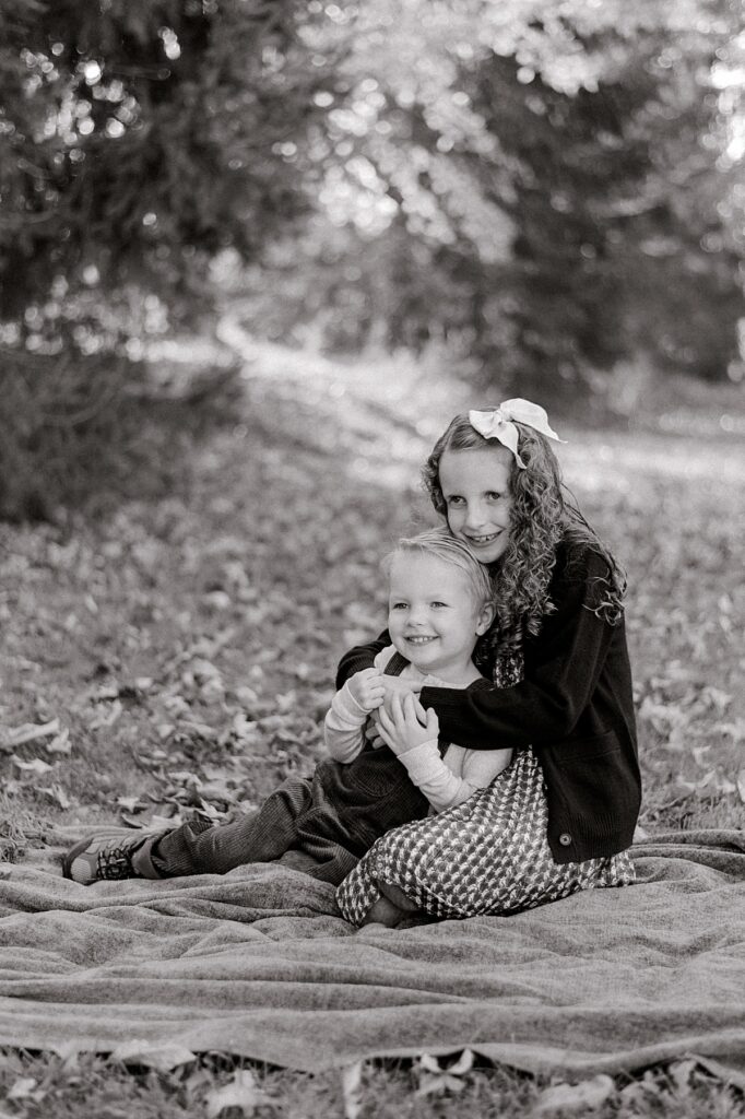 Two young siblings, sitting on a blanket, snuggling and holding onto one another while they look off camera towards their parents by Bay Village Fall Photographer, Brittany Serowski Photography.