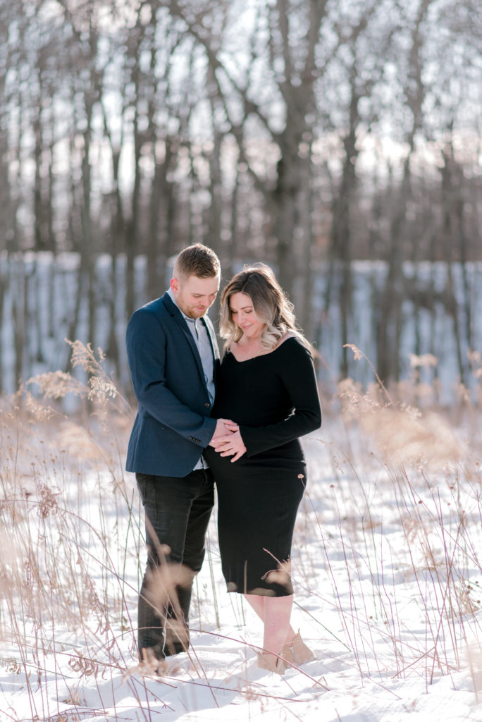 Two expecting parents holding onto the mom's pregnant belly while standing in the snow looking at her belly, by Cleveland Maternity Photographer, Brittany Serowski Photography.