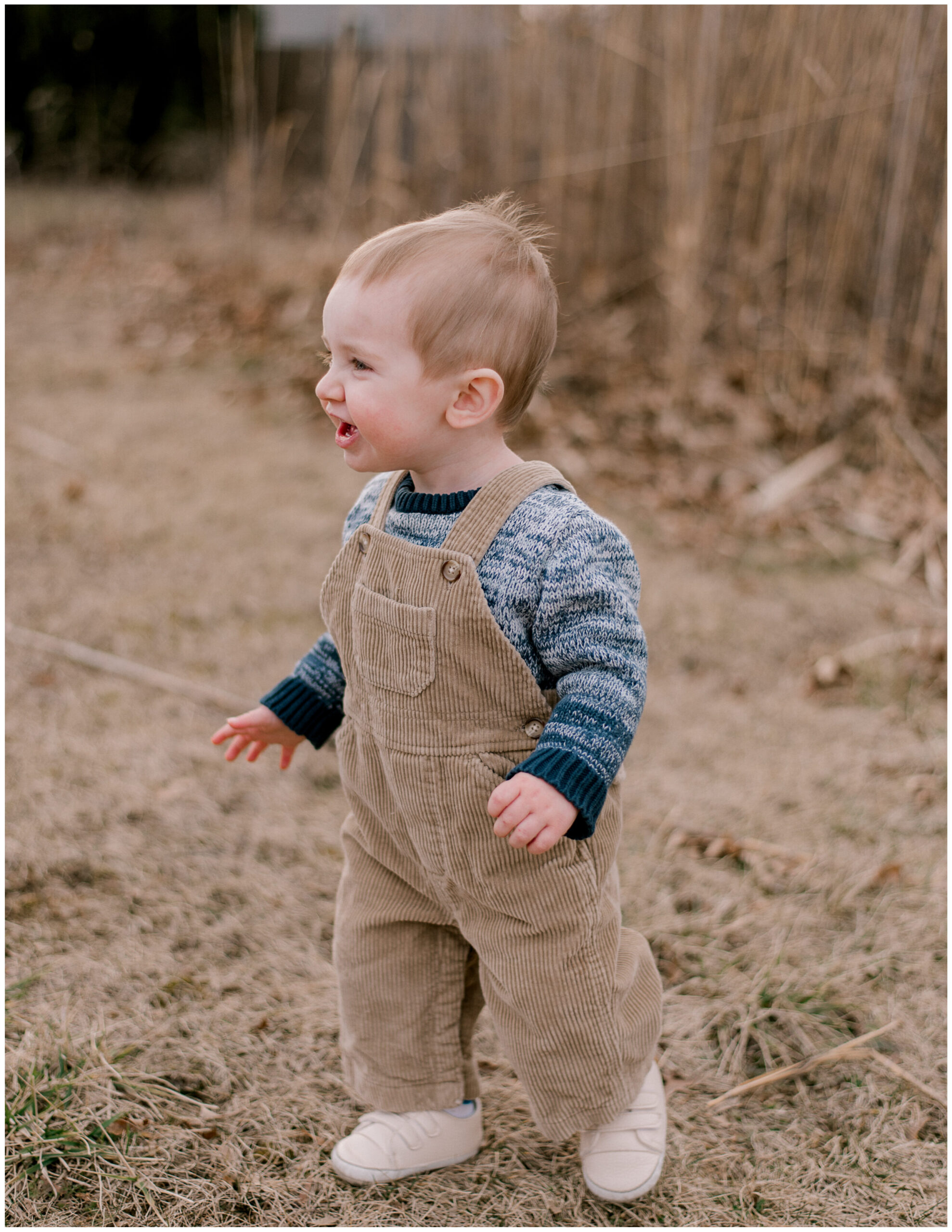 A one year old boy in corduroy overalls and a blue sweater, smiling off camera for a one year milestone session by Cleveland Family Photographer, Brittany Serowski Photography.