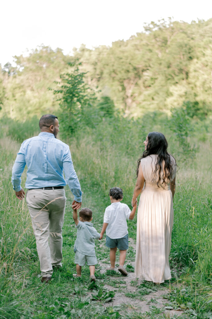 A family of four in cream and blue outfits walking away from the camera in an open field while mom and dad smile and look at each other by Brittany Serowski Photography for her Fall & Holiday Cleveland Minis.