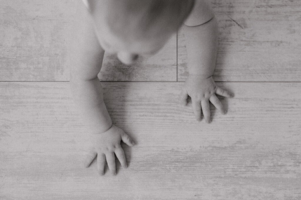 A black and white photo of a baby's hands on the ground as they are getting ready to crawl. Photographed by Cleveland Milestone Photographer, Brittany Serowski Photography.