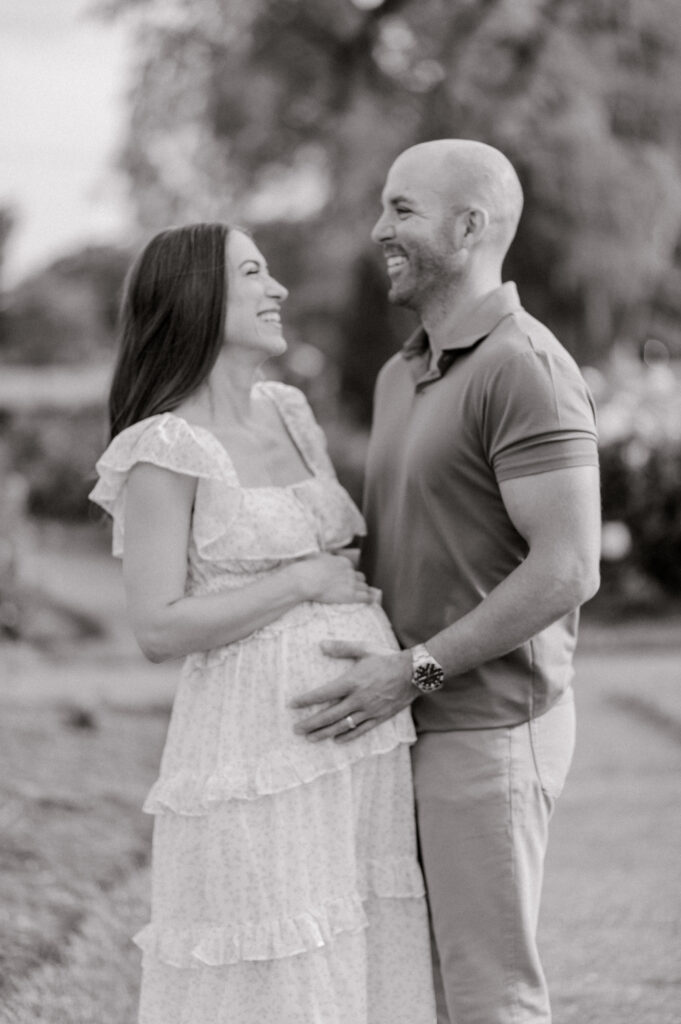 A black and white photo of newly expecting parents laughing as they embrace one another while holding onto mom's growing belly bump. Captured by Cleveland Maternity Photographer, Brittany Serowski Photography.