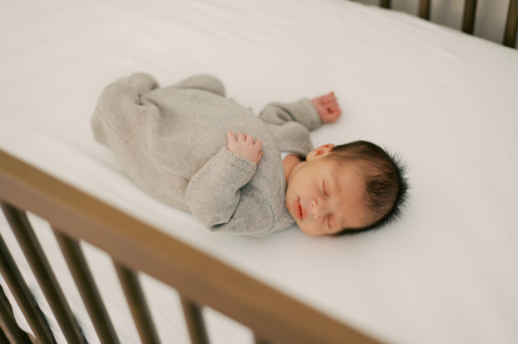 Close-up of baby laying a white and neutral crib during in-home Cleveland session. Photographed by Brittany Serowski Photography.