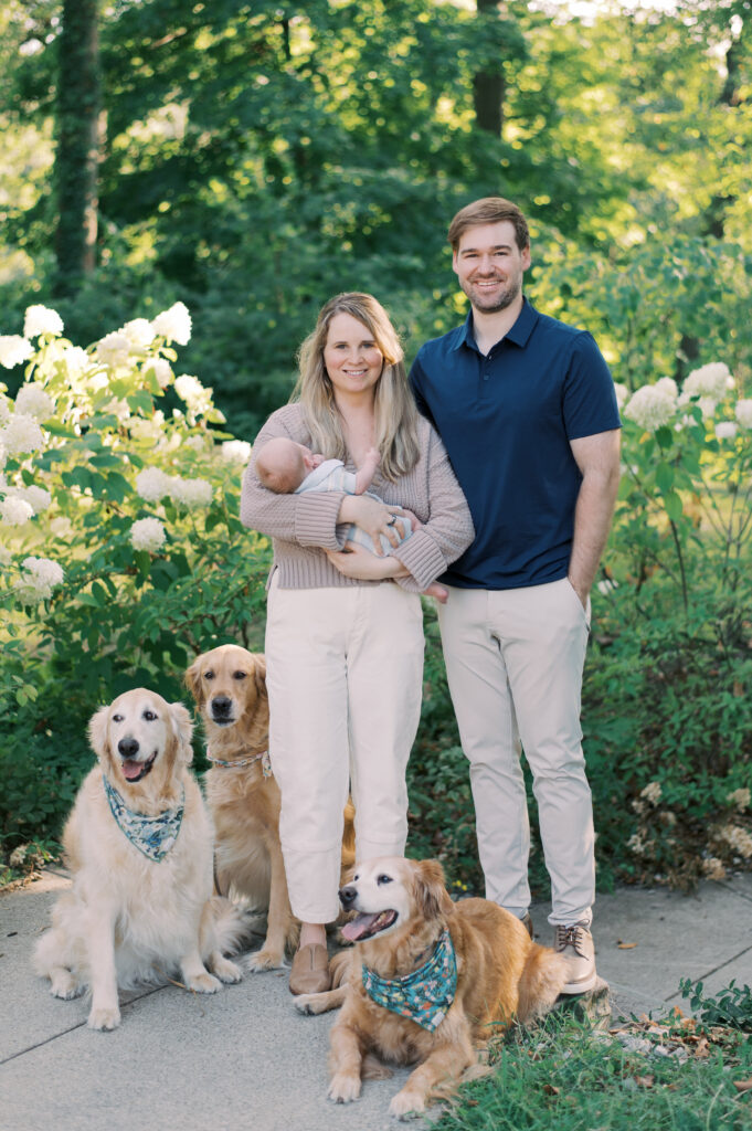 A young family, standing in front of white hydrangea bushes at the Cleveland Cultural Gardens in Cleveland, OH for spring family photos. Captured by Cleveland Family Photographer, Brittany Serowski Photography.